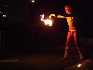 Blond guy spins fire on rooftop in socks and underwear